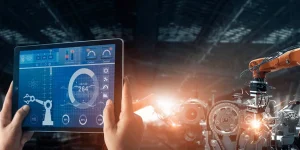 A first-person view of a person holding a tablet that displays a real-time diagnostic dashboard. In the background, a robotic arm performs precision welding on an automotive assembly line.