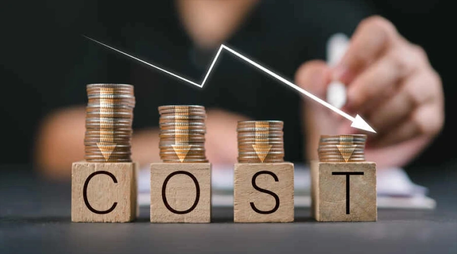Four stacks of coins sitting on wooden blocks that spell out "COST," with a white arrow pointing downward to indicate a reduction in spending.