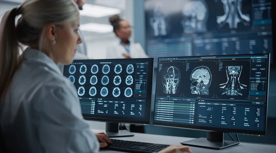 A medical doctor reviewing brain MRI scans on computer monitors.