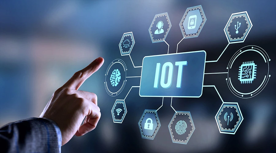 A hand pointing toward a digital interface showing a central "IOT" icon connected to various smart device and security symbols.