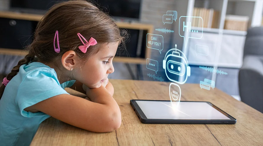 A young girl sitting at a table looking at a glowing AI chatbot graphic projected above a digital tablet.