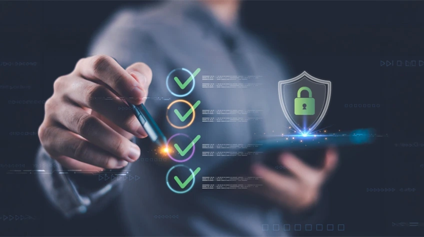 Cybersecurity Checklist for Small Businesses - WeeTech Solution Pvt Ltd Person using a stylus to complete a digital checklist next to a glowing security shield with a padlock.